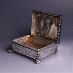 Victorian silver tobacco box, rectangular form, hinged lid embossed with a gaming scene, the body engraved with scrolls and flowers, upon four scrolling mask feet, hallmarked George Heath London 1885, H4.5cm, W10.5cm