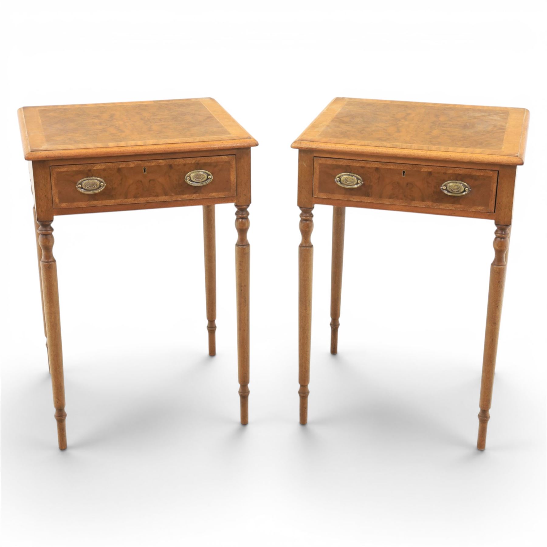 Traditional design pair of walnut lamp tables, figured top with crossbanded edge, above a single frieze drawer with brass oval handles, raised on turned supports