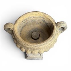 Pair of Neoclassical design weathered cast stone garden urns of kylix form, the rolled rim flanked by twin pierced scroll handles over a shallow gadrooned bowl, raised on a fluted circular socle and faux panelled square pedestal base