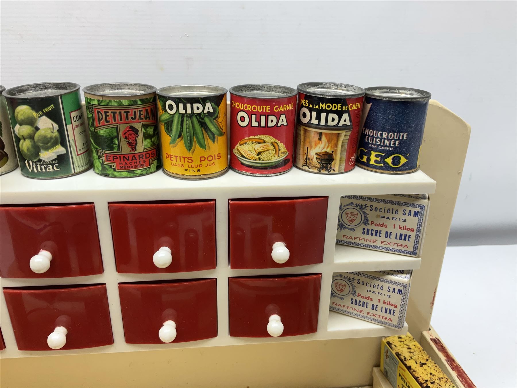 Late 1950s continental red and white painted wooden diorama of a grocery shop interior with fitted shelves and drawers and freestanding 'glazed' counter, fully stocked with miniature tin cans and packets of food L42cm H23cm D22cm
