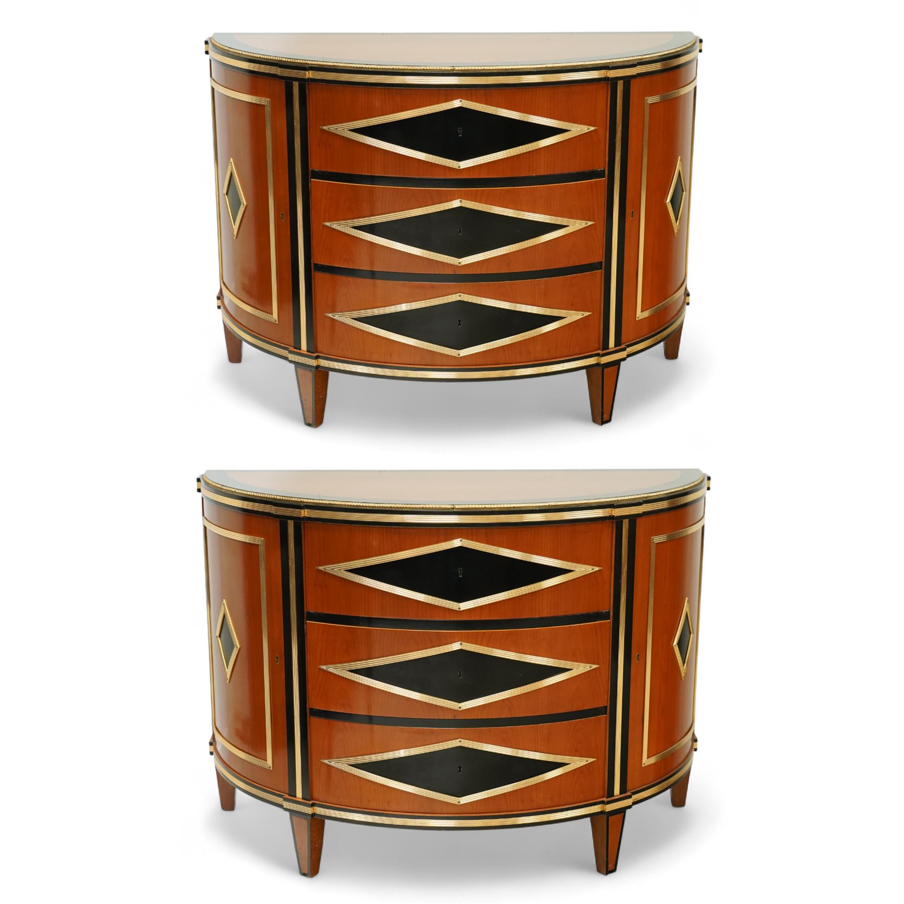 Colombo Mobili - Pair of Italian designer cherrywood art-deco inspired demi-lune commode cabinets, the shaped top with ebonised inlay and gilt brass repeating anthemion beading above a gilt brass reeded moulding, over three long drawers with gilt brass geometric panel mounts, flanked by cupboard doors with diamond motif, raised on tapering square supports 