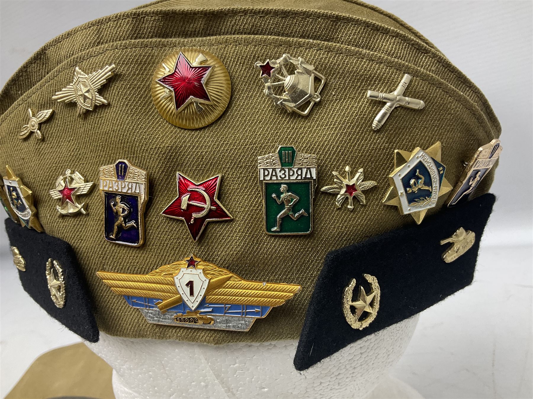 Four side caps - WW2 Russian, post-WW2 Russian and two East German; all with badges, one with multiple metal badges (4)