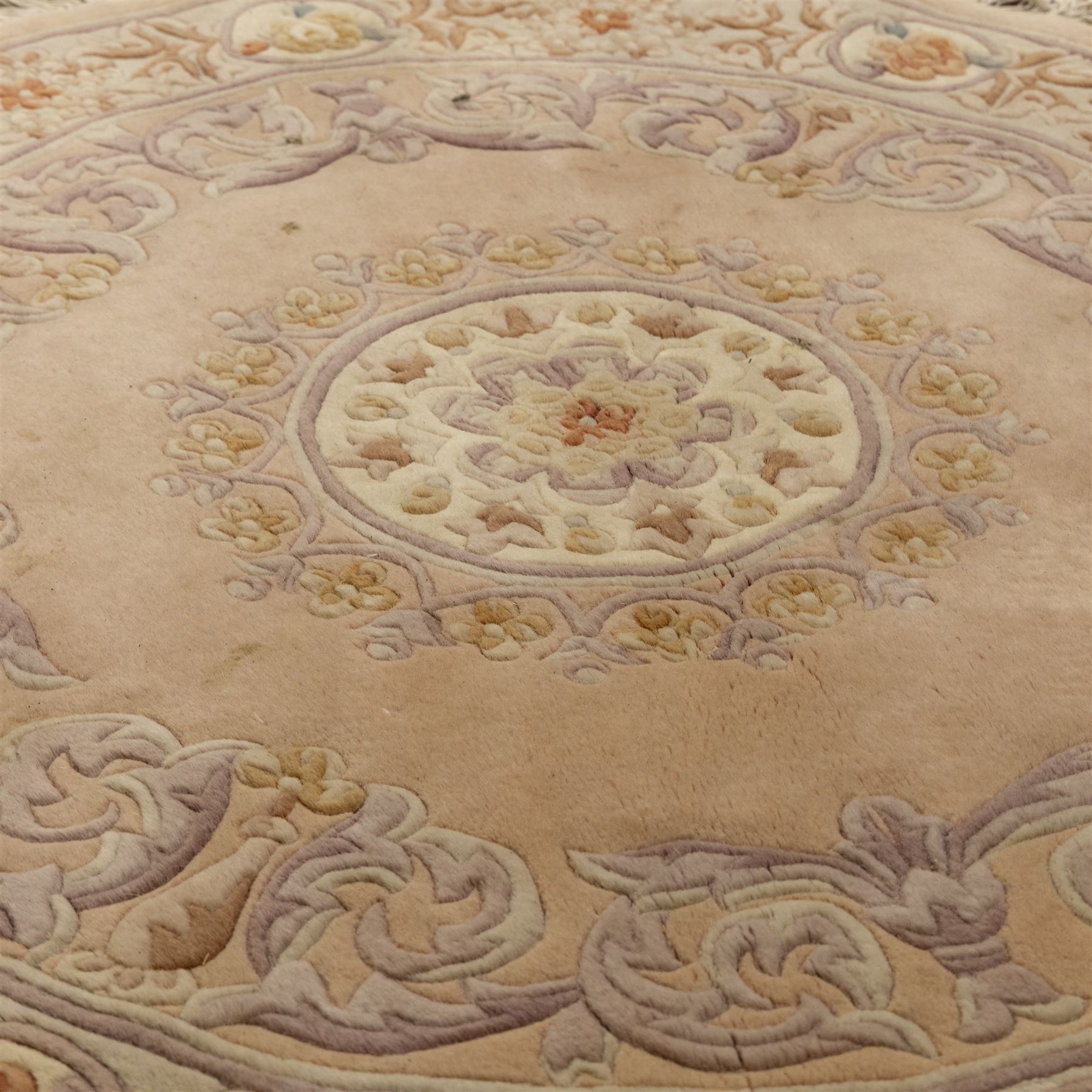 Late 20th-century circular peach-toned rug, with central floral rosette medallion surrounded by scrolling floral motifs within concentric borders, with cotton fringe perimeter 