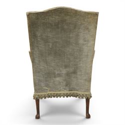 Pair of Georgian style wing armchairs, upholstered in green velvet, each with shaped wing backs, padded scroll arms and loose seat cushions, raised on cabriole supports terminating in pad feet, one with tasselled fringe