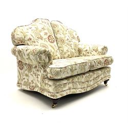 Pair traditional shaped two seat sofas upholstered in floral pattern and cream ground fabric, turned front supports with brass castors 
