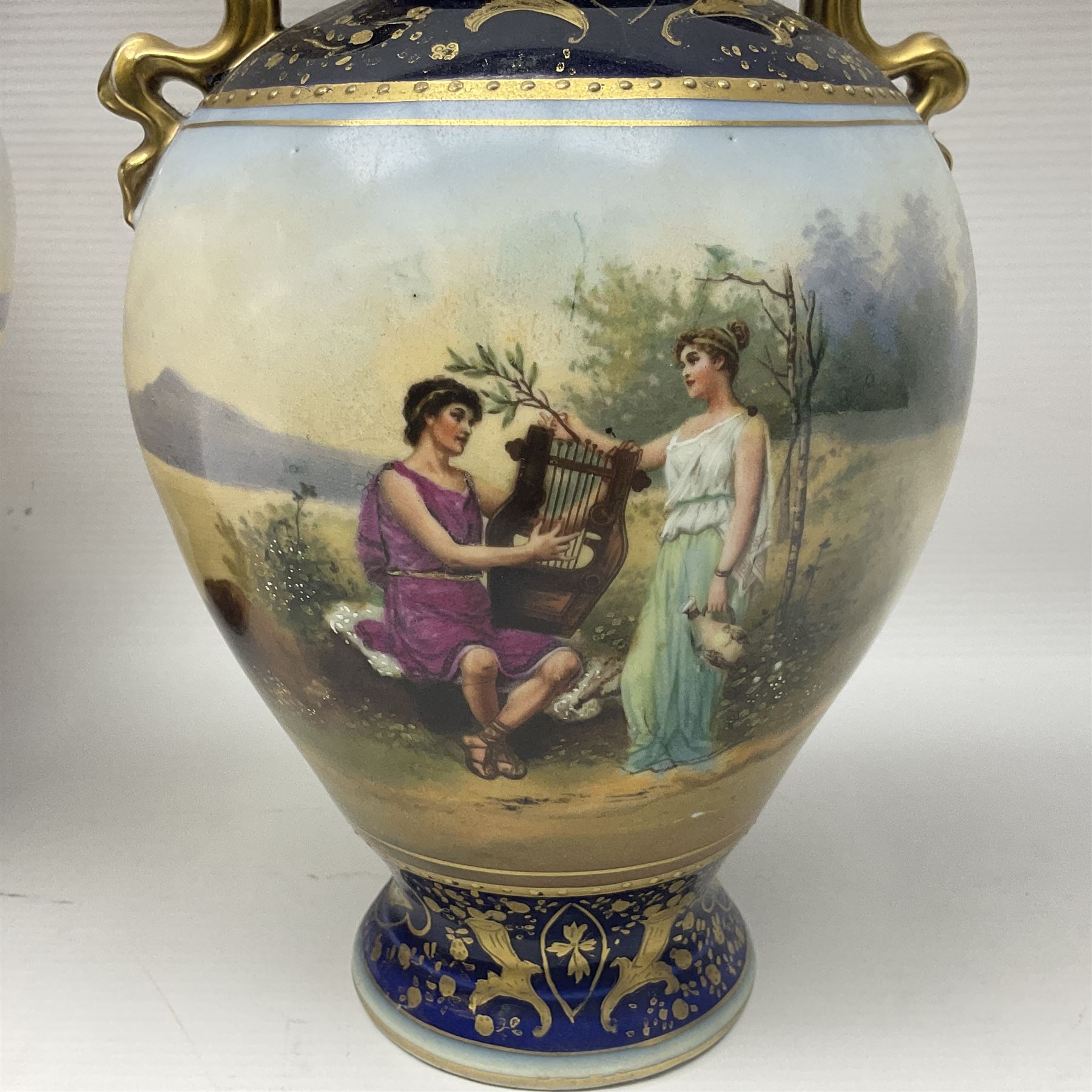 19th century Vienna style porcelain 'Musik' garniture, the central vase of baluster form with domed cover flanked by two smaller vases with twin curved gilt handles to short neck, each decorated with classical figural vignettes between blue borders heightened with gilt, H33.5cm