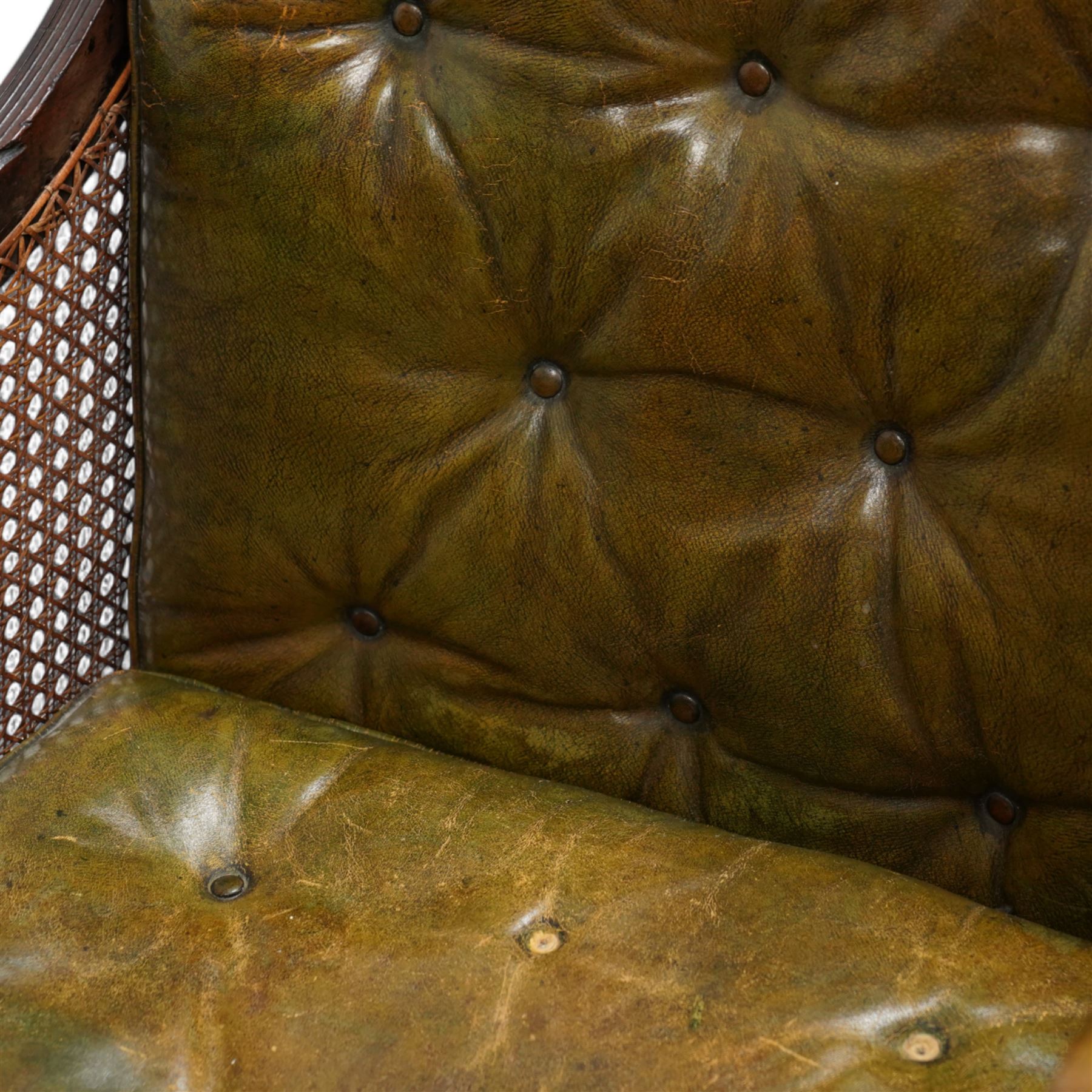 George IV mahogany framed library reading chair, reed moulded frame with cane work seat, back and sides, with loose cushions upholstered in green buttoned leather, upholstered arm rests, turned arm supports terminating to turned and reed carved feet, on castors 