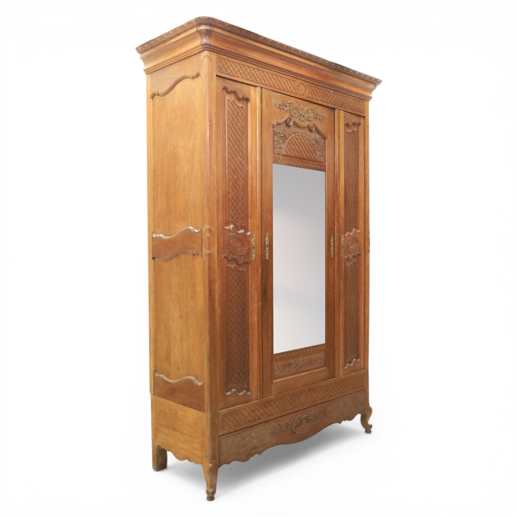 Early 20th century French oak triple door armoire, the moulded top above a frieze with carved lozenge decoration and central rosette, the central mirrored door enclosed by carved surround with floral crest, flanked by panelled doors with lattice carving, the base with shaped apron centred by carved basket motif, upon shaped cabriole supports