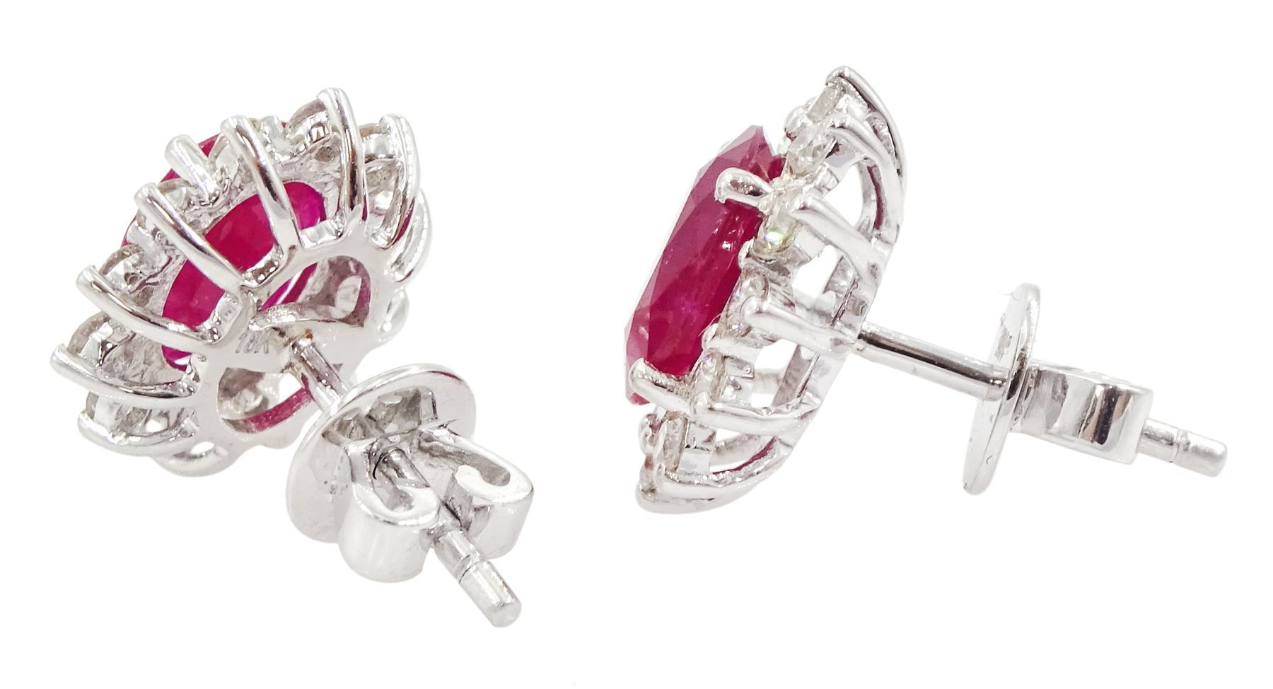 Pair of 18ct white gold ruby and diamond earrings, each stud set with a single oval cut ruby, surrounded by twelve round brilliant cut diamonds, stamped, total ruby weight approx 3.10 carat, total diamond weight approx 0.50 carat