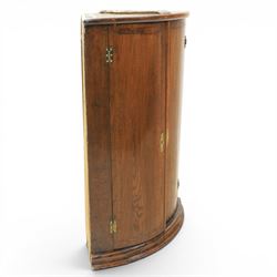 George III oak cylindrical corner cupboard, bow fronted doors revealing a painted shelved interior, brass escutcheons  and hinges, raised on a moulded plinth base