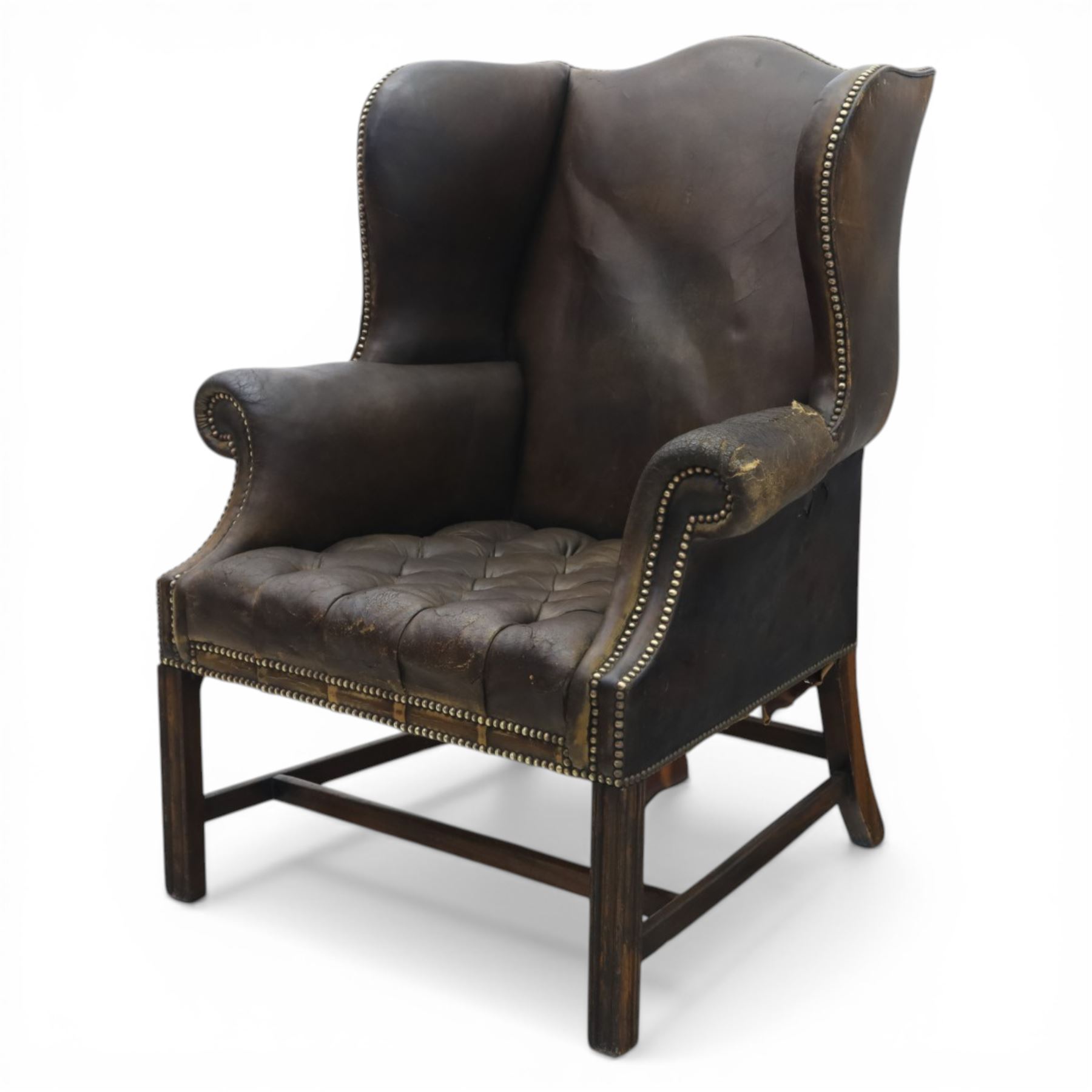 Georgian style leather wing armchair, shaped high back with outscrolled wings above padded arms and deep buttoned seat, close-nailed throughout, raised on square supports united by H-stretcher