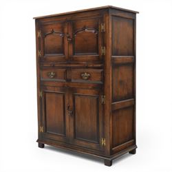  Late 20th century oak four door cupboard in the manner of Titchmarsh and Goodwin, rectangular plank top above two pairs of fielded panel doors with shaped raised panels, central arrangement of a brushing slide above two short drawers with brass swan neck handles and pierced backplates, enclosed by further pair of panelled cupboard doors, fitted with brass butt hinges and turned wooden knobs, raised on plinth base