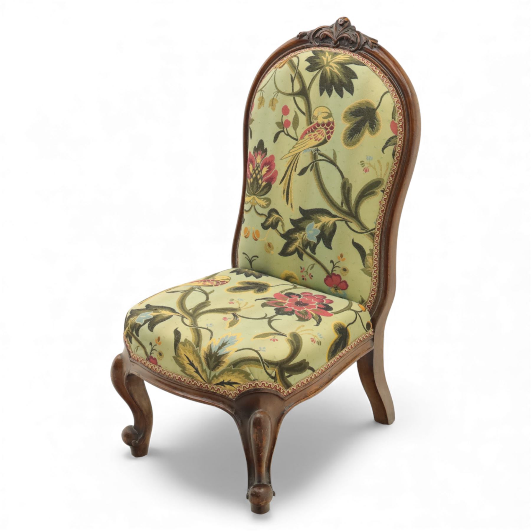 Small Victorian mahogany nursing chair, with carved top rail above a padded balloon back and shaped seat upholstered in light green fabric detailed with exotic birds and flowering vines, raised upon cabriole front legs and turned rear supports