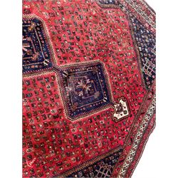 Persian crimson ground carpet, the field decorated with an indigo triple lozenge pole medallion, surrounded by all-over Boteh motifs, the guarded border with repeating geometric and floral designs