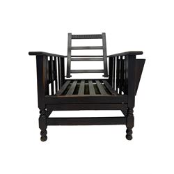 Late Victorian oak steamer chair, adjustable slatted backrest with grooved crest rail, wide armrests extending to a sliding adjustable footrest, open frame sides with vertical slats, side magazine rack and collapsible table, raised on turned front supports