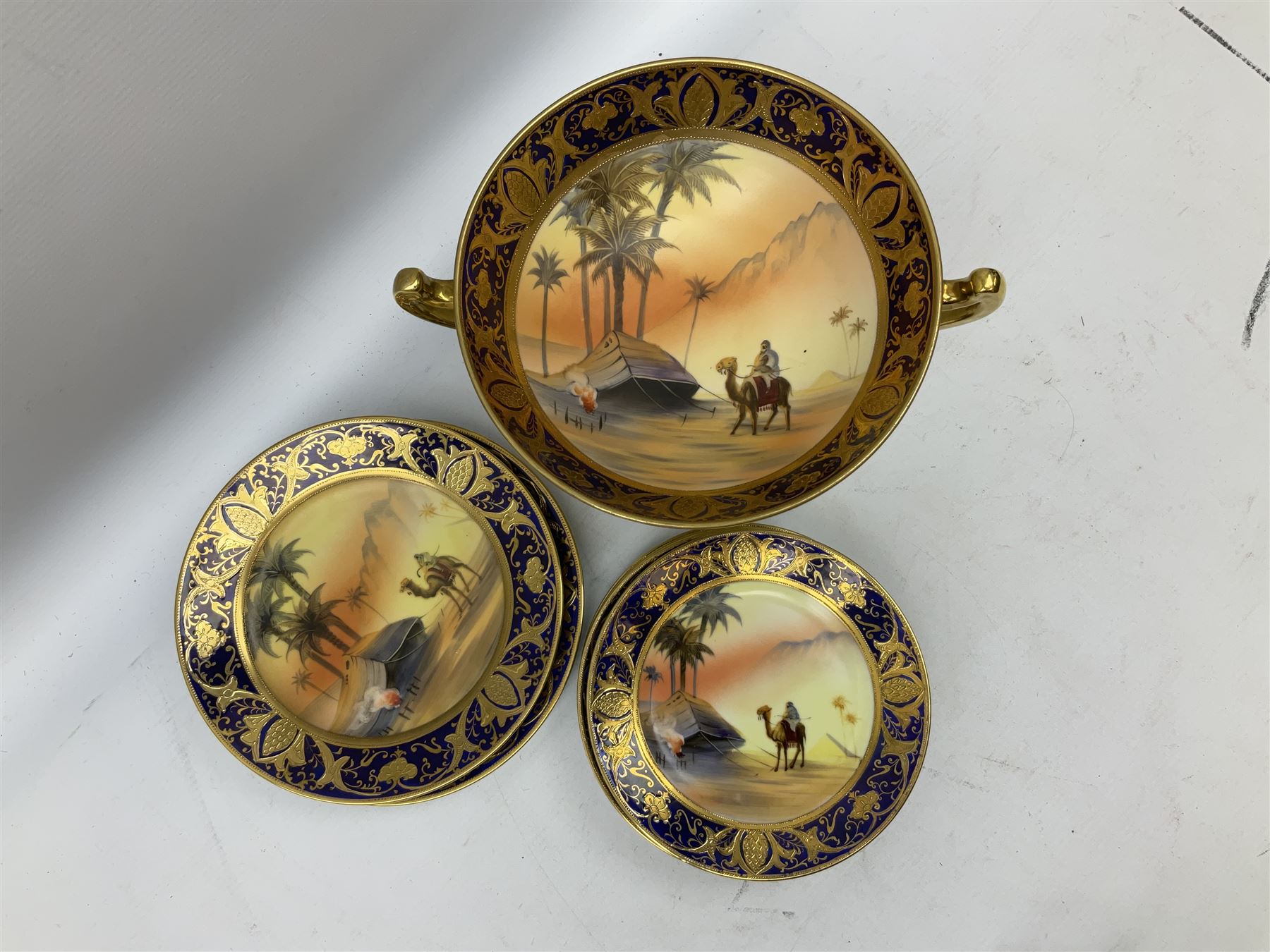 Noritake tea service for four, decorated with desert camel scene with blue border and gilding, comprising four teacups and saucers, four side plates, lidded sucrier, teapot and jug, together with twin handled pedestal bowl etc (19 pcs) 
