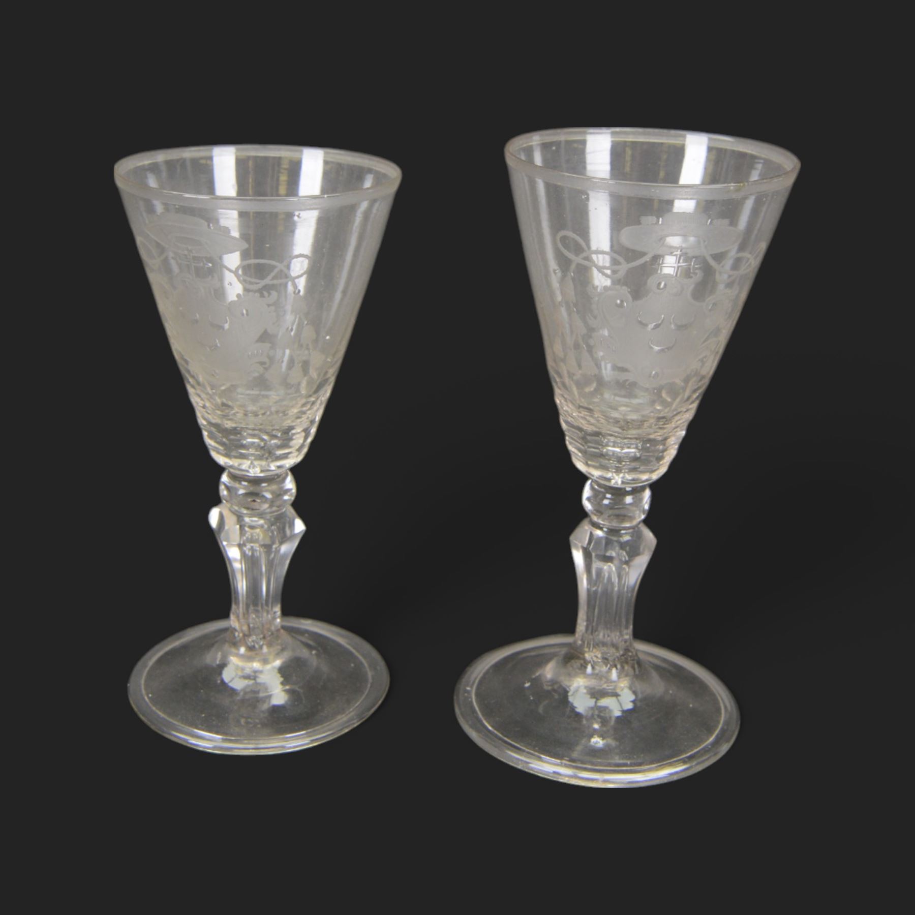 Two 18th century Continental facet cut drinking glasses, each with funnel bowl engraved with armorial type cartouche, upon a knopped and facet cut stem with internal elongated tear, and spreading folded foot, largest H15.5cm