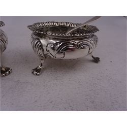 Pair of Edwardian silver open salts, of cauldron form, repousse embossed with flower heads and upon three paw feet, hallmarked London 1904, maker's mark worn and indistinct, together with a pair of silver salt spoons, hallmarked Broadway & Co, London 1906
