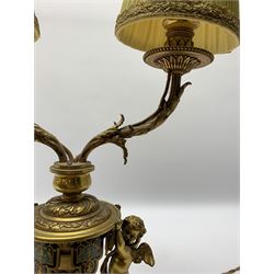 19th century French ormolu and champlevé twin branch table lamp, the stepped plinth base supporting an urn shaped body flanked by two putto, with twin acanthus detailed branches with foliate and beaded drip pans and sockets, with pleated gilt trimmed shades, including shades H47cm