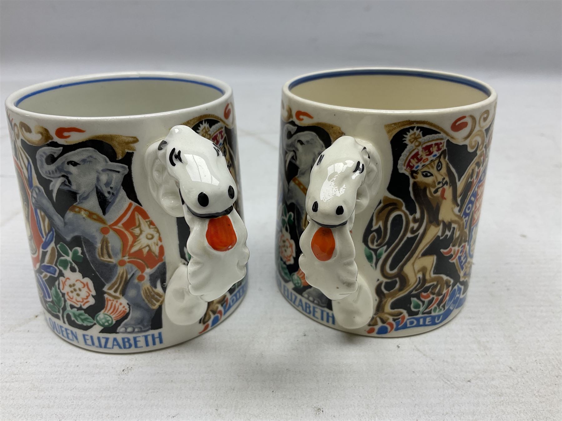 Two Dame Laura Knight coronation mugs for King George VI and Queen Elizabeth, comprising a Burleigh Ware example and a J&G Meakin example, each with a lion moulded handle and printed marks beneath, H8cm