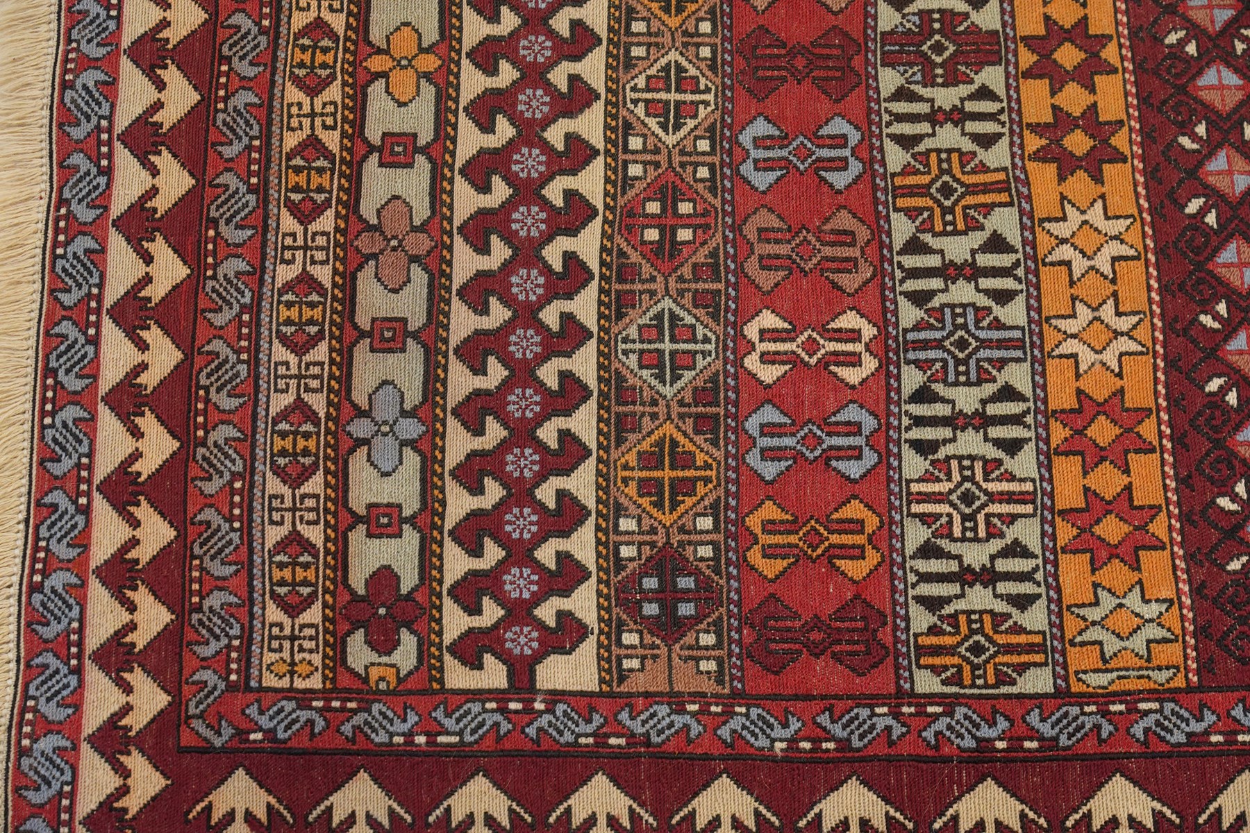 
Oman tribal design rug, field decorated with horizontal bands of stylised birds, flowerheads, stars and hooked geometric motifs in red, ivory, ochre and pale blue, enclosed by serrated ivory and red borders and narrow patterned guard stripes