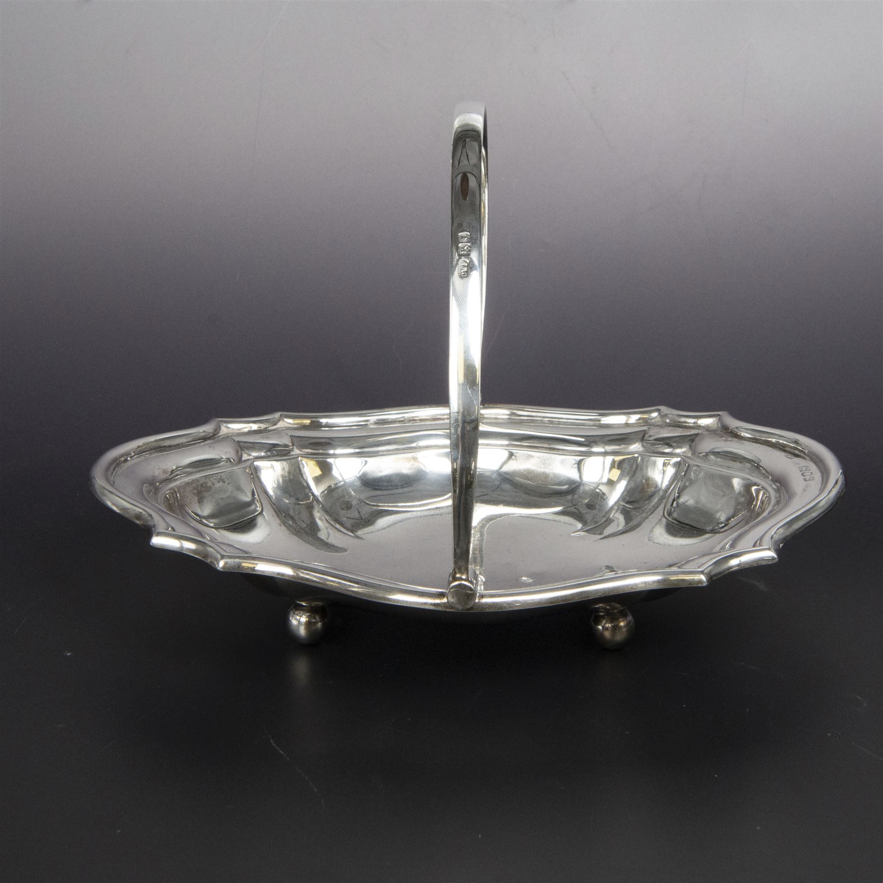 Early 20th century silver swing handled basket, of oval form with shaped rim and upon four bun feet, hallmarked C W Fletcher & Son Ltd, London 1918