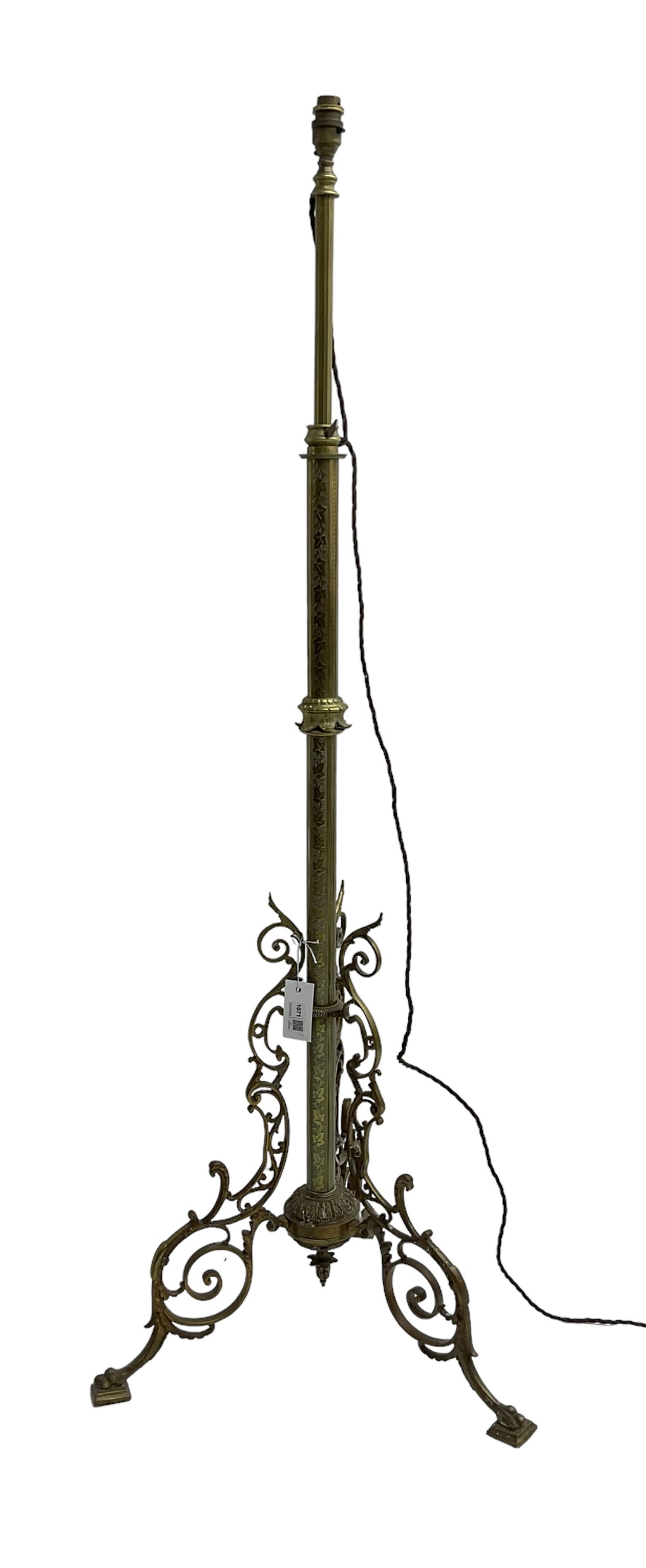 Victorian brass floor standing oil lamp, column decorated with ivy and acanthus leaves, the tripod base pierced with scrolled foliate decoration, with ivory and gilt shade, later converted to electricity