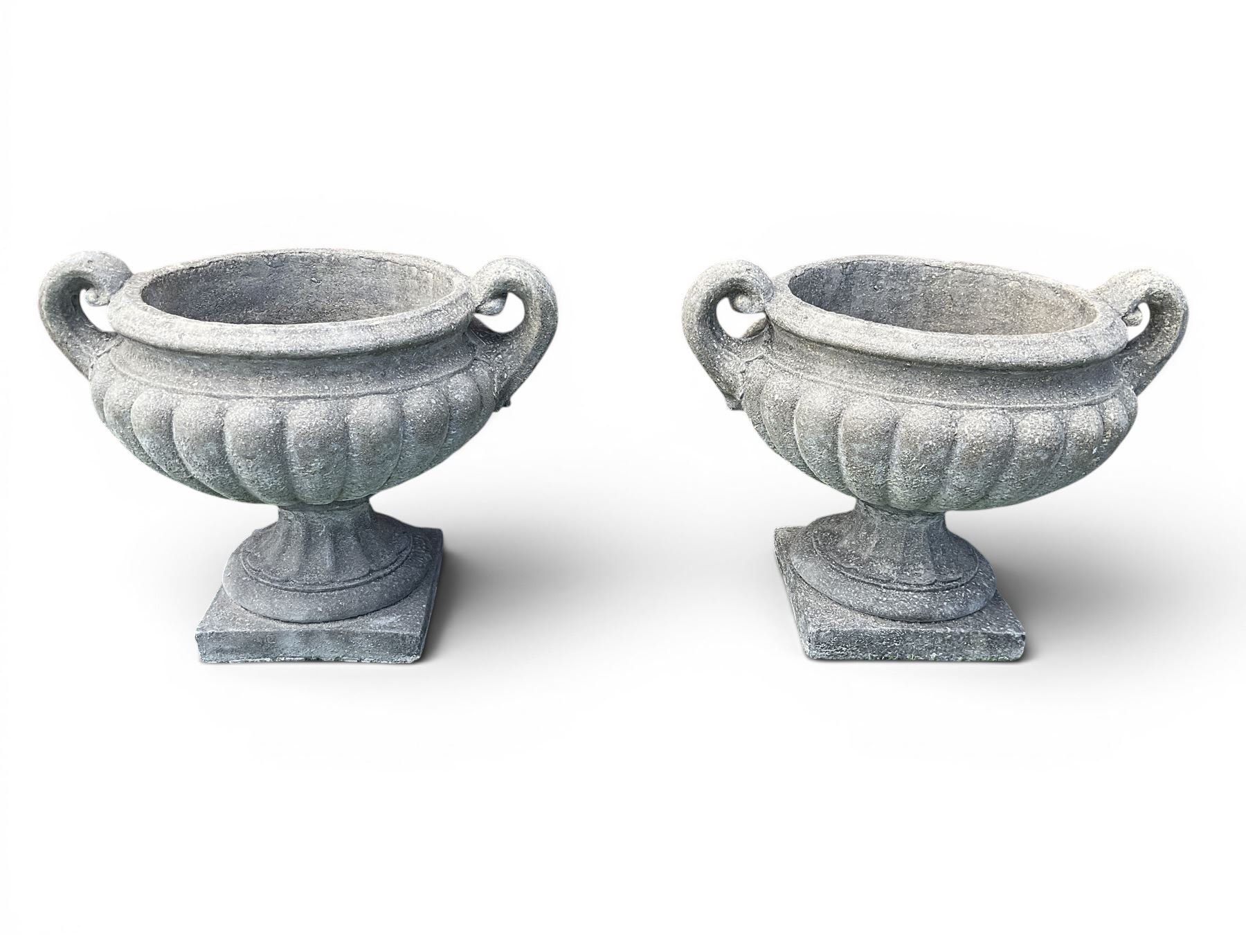 Pair of squat cast stone garden urns of kylix form, gadrooned body with twin pierced scrolling handles, fluted socle on square base