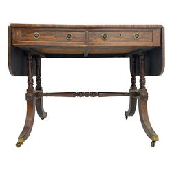 Regency rosewood sofa table, drop leaf rectangular top with rounded corners, fitted with two drawers and two opposing false drawers, raised on dual turned columns terminating in splayed feet united by turned stretcher, on brass cups and castors
