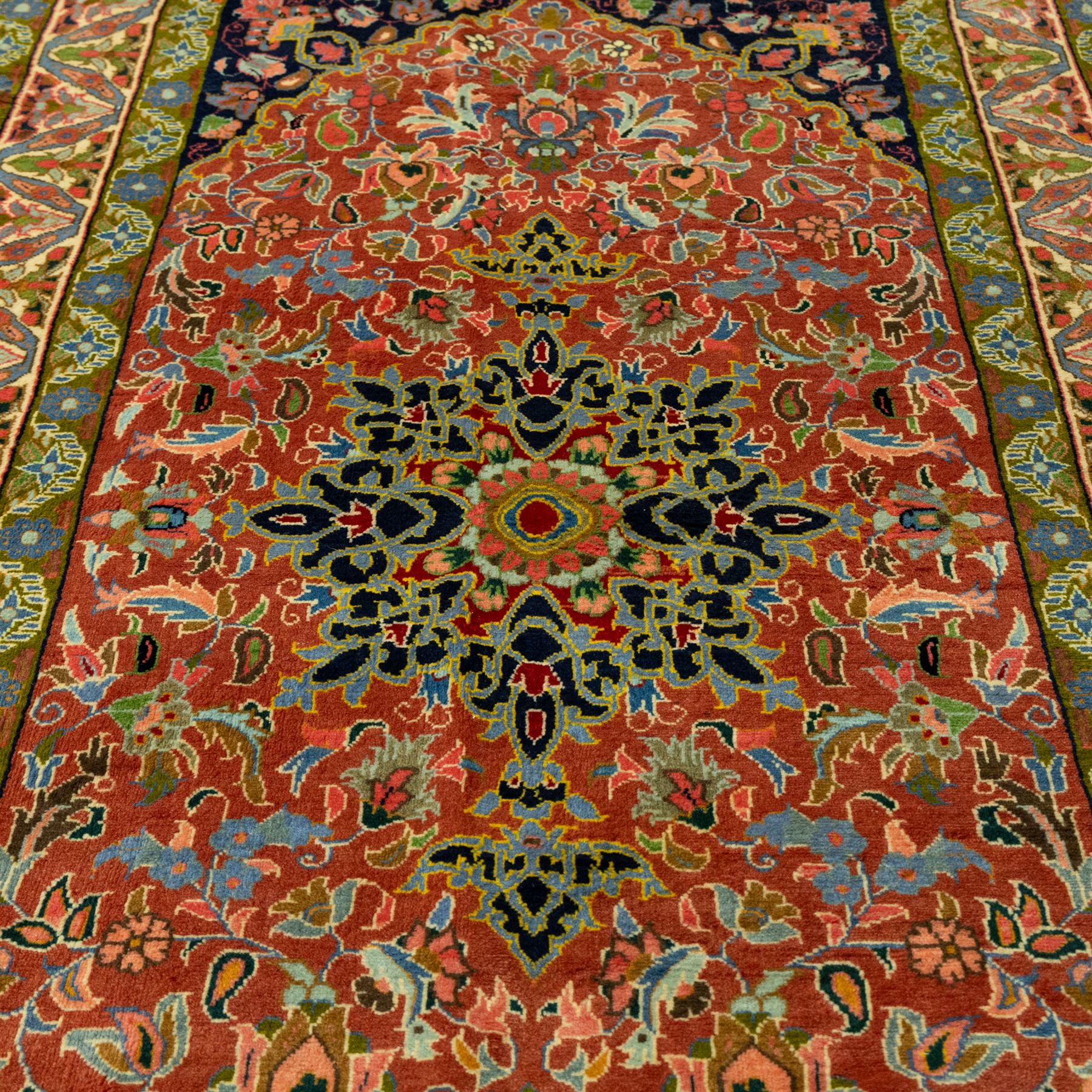 South Persian Sirjan hand-knotted carpet, terracotta ground, with a central shaped dark navy floral medallion with pendants, surrounded by scrolling foliate and floral motifs incorporating palmettes, rosettes and stylised vine work in blue, green and ivory tones, enclosed by dark navy spandrels and a wide green and ivory border with repeating palmettes and angular leaf motifs, flanked by patterned guard stripes, with cotton fringes