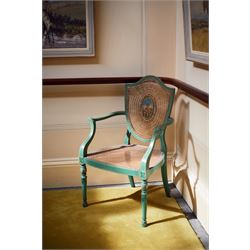 Pair of Edwardian Hepplewhite Revival green-painted open armchairs, cane work shield back with central oval panel panted with putto set upon rocky landscape with water and trees, shaped and rolled arms enclosing cane work seat, on turned front supports decorated with acanthus leaves and draped festoons 