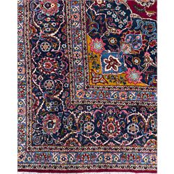 Central Persian Kashan hand-knotted carpet, madder red field with an intricate design of scrolling vines, palmettes, and rosettes with a central lobbed medallion with pendant motifs in shades of blue and ivory, and spandrels all within a blue-ground border of palmettes and flowerheads between multiple guard borders, 450cm x 335cm 