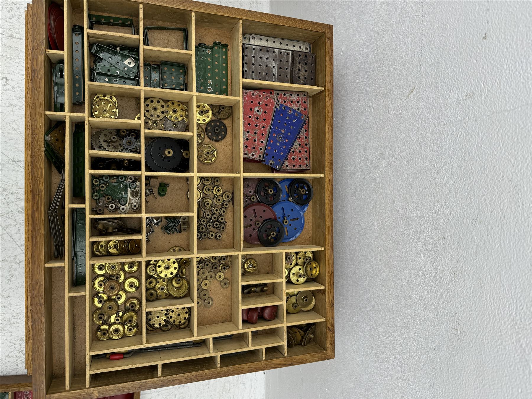 Large collection of Meccano, including perforated strips, wheels, cogs, nuts and bolts, various Meccano instruction manuals and magazines, all housed within a modified wooden box, with three tiered compartmentalised sections and upon four twist legs, box H60cm