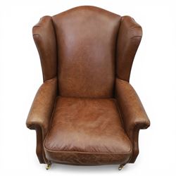 Laura Ashley - Pair of brown leather wingback armchairs, with scrolled arms and loose cushion seat, brass studded trim, on cylindrical tapering legs terminating in castors