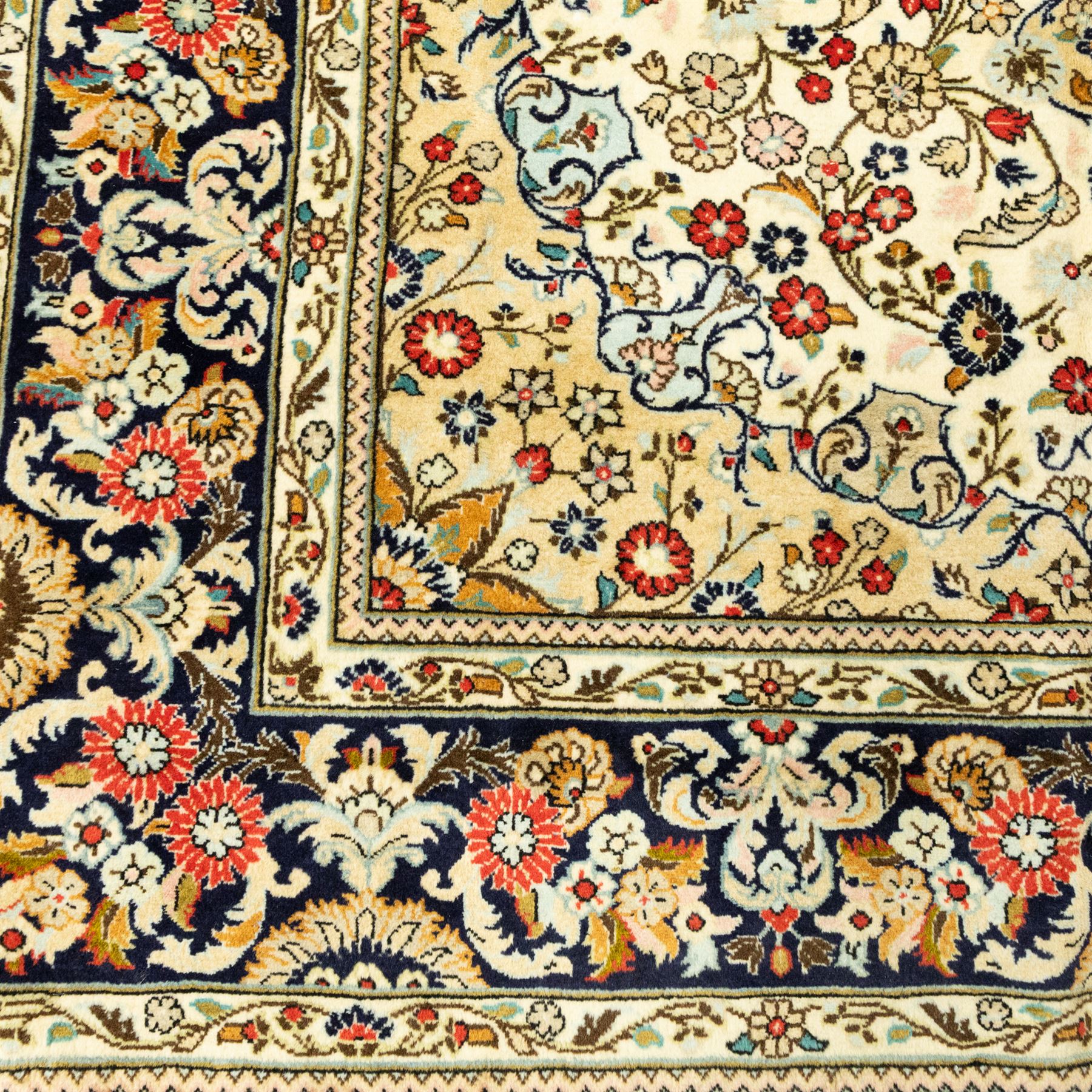 Central Persian Kashan hand-knotted carpet, ivory ground, with an all-over floral field centred by a subtle shaped medallion, surrounded by scrolling foliate and floral motifs incorporating rosettes, palmettes and delicate vine work, enclosed by a dark navy border with repeating palmettes and meandering vines, flanked by floral guard stripes, with cotton fringes