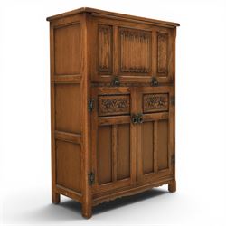 Old Charm - carved oak bar with three bar stools and associated Old Charm drinks cabinet, carved top with channels for glassware beneath, bar surface above glazed panels, shelves for glassware to the back, associated Old Charm drinks cabinet with fall front linenfold carving, above twin doors with shelved interior