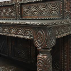 An early 20th-century Jacobean revival style carved oak Court Cupboard, tier-form of 17th-century design, rectangular form with carved back with geometric motifs and arches, projecting top section over twin baluster columns connecting the lower tier above a carved panelled front and panelled cupboard door with profusely carved lozenges and lunettes, above two base drawers, raised on block feet 