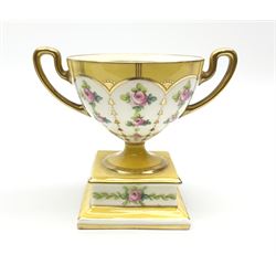 An early 20th century Minton pedestal cup with twin handles, decorated with hand painted roses and gilt husks within yellow borders, with printed mark beneath, H11cm. 