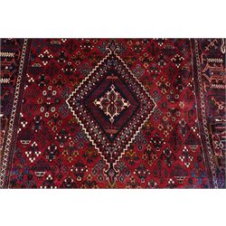 Central Persian Joshaghan hand-knotted carpet, deep red field decorated with a lattice design of stylized boteh and palmette motifs arranged around a stepped diamond medallion, navy corner spandrels similarly decorated enclosed by a dark indigo main border of floral and geometric motifs between multiple guard stripes, with cotton fringe ends 