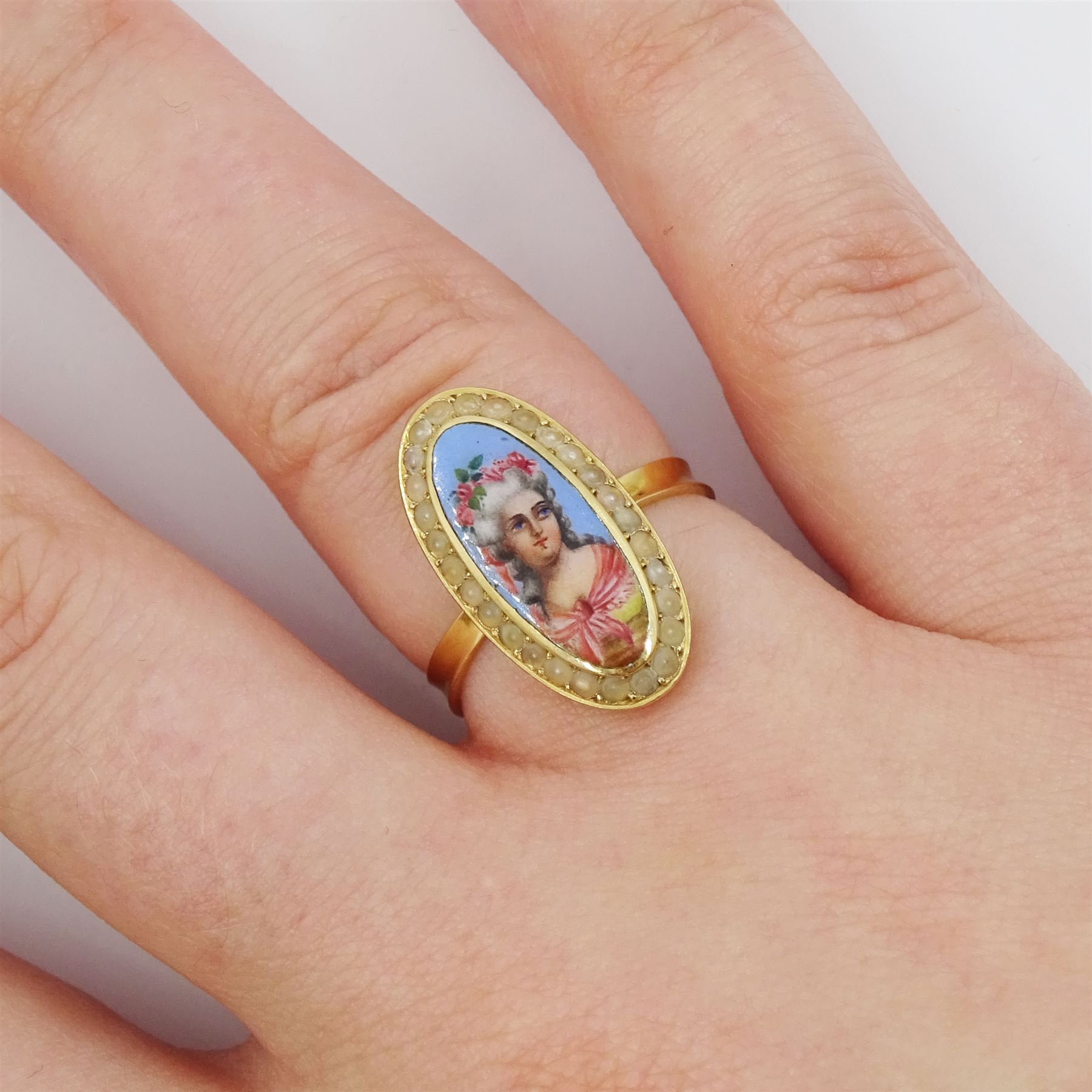 19th century French gold pearl and enamel portrait ring, set with an oval hand painted enamel portrait of a woman wearing a pink shawl and flowers in her hair, surrounded by seed pearls