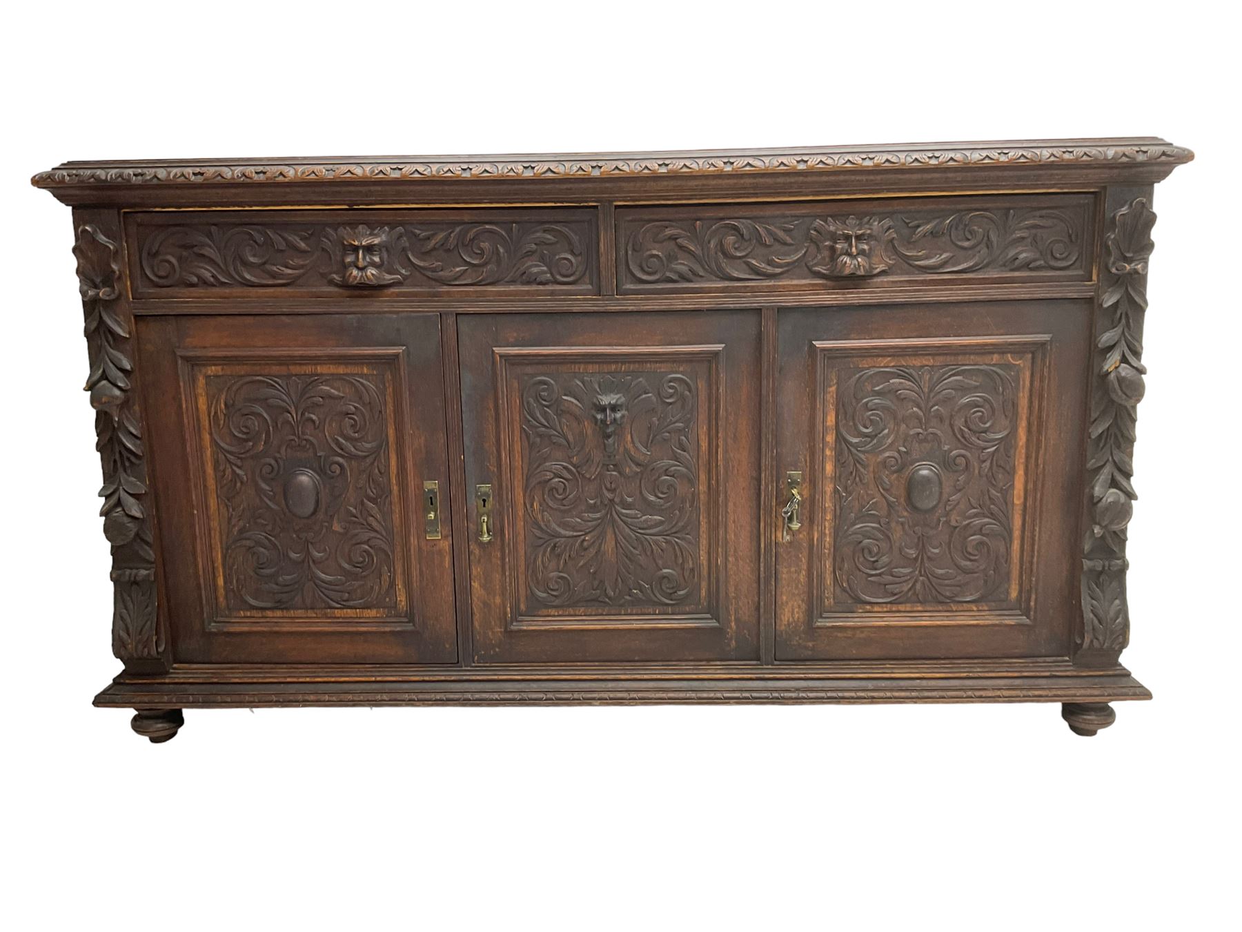 Victorian heavily carved oak sideboard, the moulded top carved with foliate decoration to the edge, fitted with two drawers and three cupboards, the drawer fronts carved with green man mask handles and scrolling foliage, the panelled doors carved with interlacing foliage, on turned compressed bun feet
