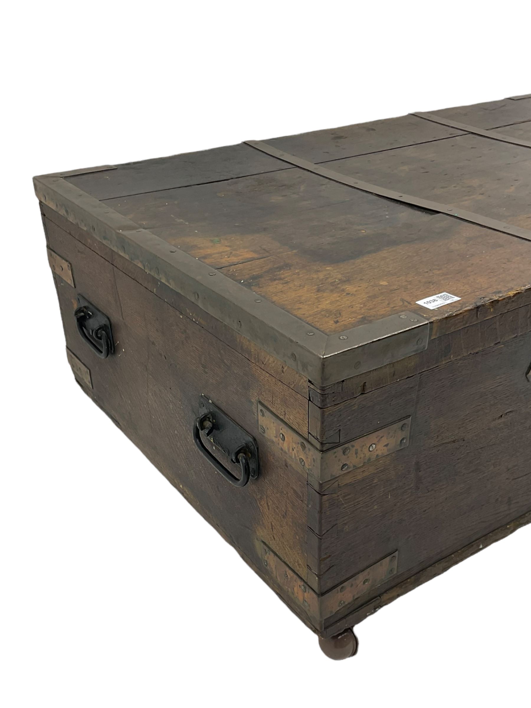 Early 19th century oak low blanket chest, metal strapped and bound, two carrying handles to either end, on castors