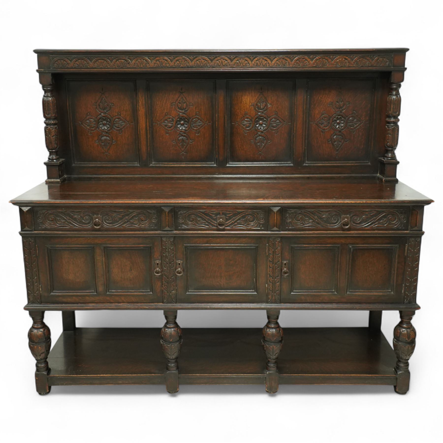 Early 20th century carved oak sideboard Jacobean style with panel back on cup and cover legs, the top section with carved panels and reeded moulding, three deep frieze drawers over triple panelled cupboard doors, raised on carved baluster legs joined by lower shelf