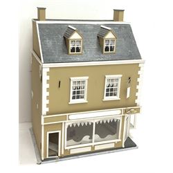A large dolls house, with shop front ground floor, and wall papered interior with curtains and fireplaces, H94cm L67cm D43.5cm.  