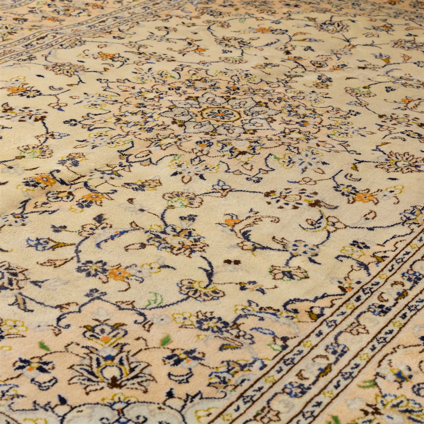 Central Persian Kashan hand-knotted carpet, ivory ground with central rosette medallion surrounded by scrolling floral vines and palmettes, field framed by a meander border flanked by multiple guard stripes, with cotton fringe end and a replaced fringe end