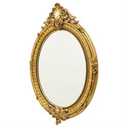 Pair of Rococo Revival gilt framed oval wall mirrors, the exuberant pediment formed of scrolling acanthus leaves and rocaille ornament, the oval bevelled plate set within with ebonised slip with outer repeating lappet decoration, over a rocaille cartouche terminal