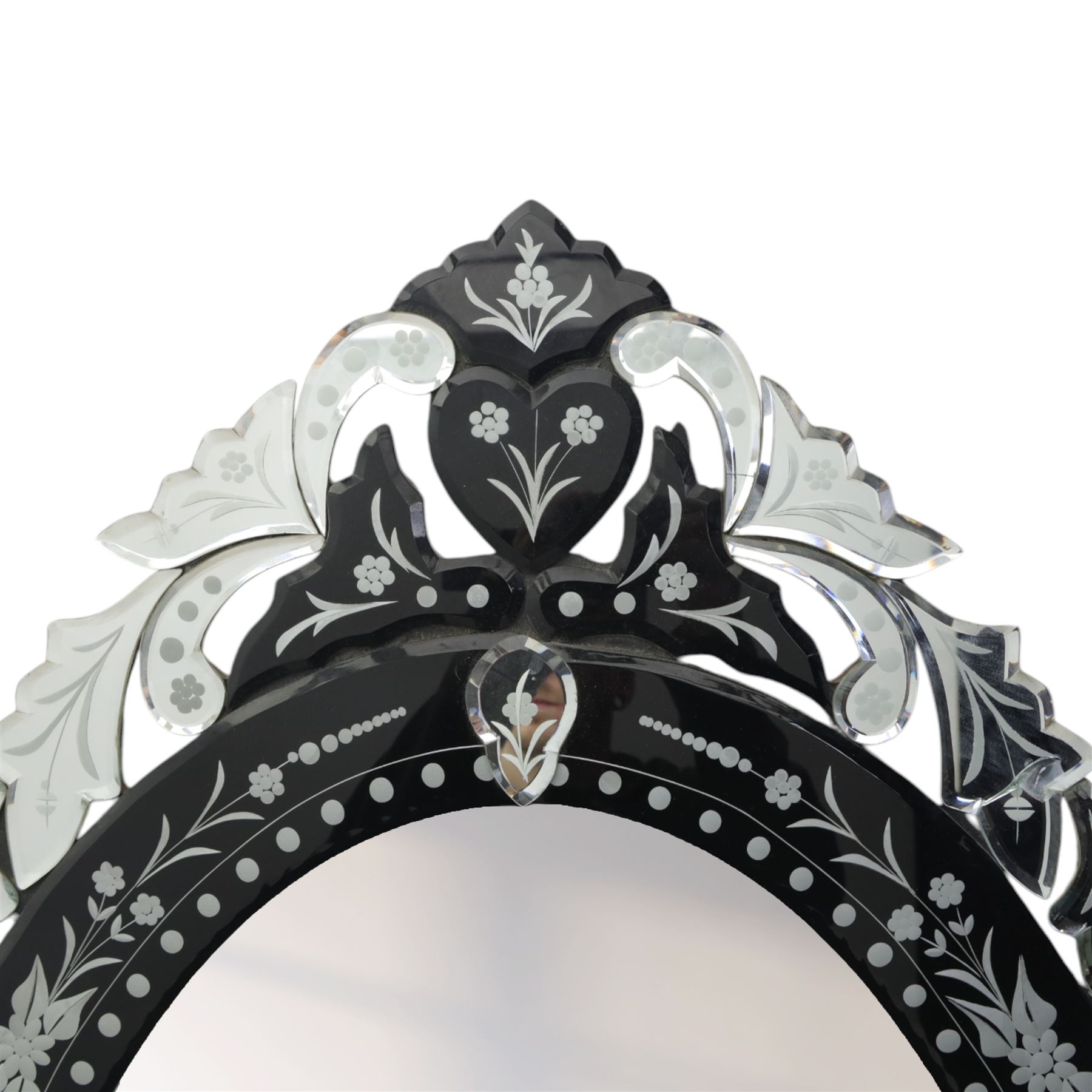 20th century Venetian style oval mirror, the central mirror plate enclosed by an ebonised border decorated with engraved floral trails and dotted reserves, the outer edge applied with shaped and etched glass leaves and scrolling foliage