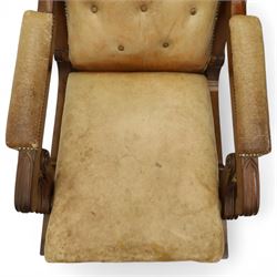 William IV mahogany gentleman's library reclining armchair, leather button upholstered and brass-studded back and seat, above leather-covered arms terminating with carved roundels and foliate scroll-carved ends, underside with brass mechanical trigger reclining lever, the apron with retractable foot rest, supported on lappet carved and turned legs with brass castors, circa 1835