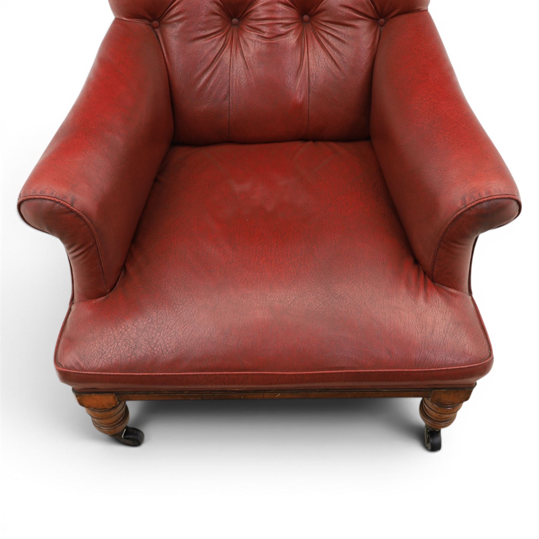Early 20th century style oxblood red leather Chesterfield armchair, deep buttoned shaped back over padded scroll arms and loose seat cushion, raised on turned mahogany front supports with brass caps and castors