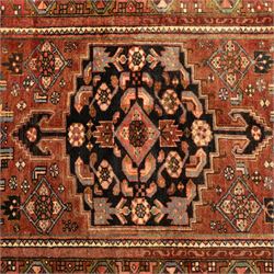 North West Persian Zanjan hand-knotted rug, madder-red field with a central stepped lozenge medallion enclosing stylized geometric floral motifs in indigo, ivory, and brown, angular spandrels filled with tribal devices and framed by a series of geometric borders with latch-hook rosette and leaf motifs, with cotton fringe ends  